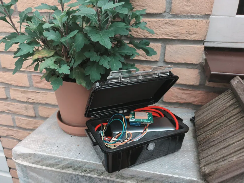 An open Peli case on a garden ledge, holding a RockBLOCK 9603, an ESP32-S3 LoRa board and a power bank